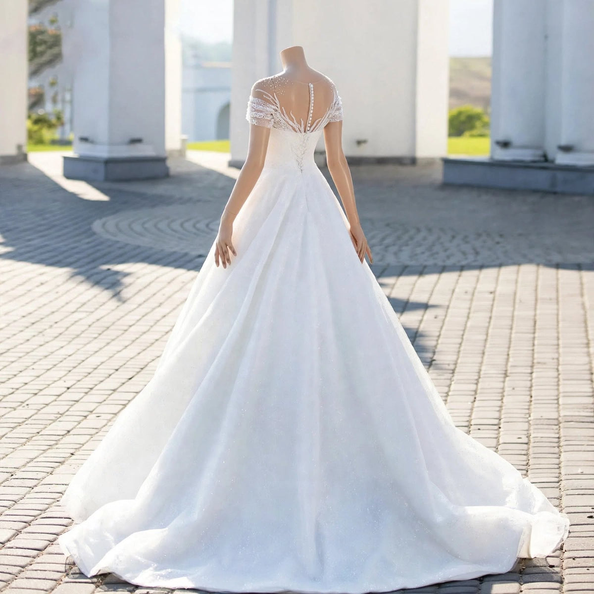 White A-line wedding dress with sheer illusion neckline, lace appliqué, pearl beading, and off-the-shoulder sleeves displayed on a mannequin.
