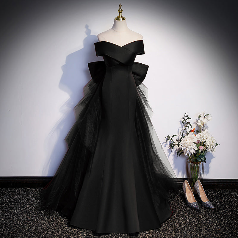 Black off-shoulder gown on a mannequin with a vase of flowers and shoes on the floor.