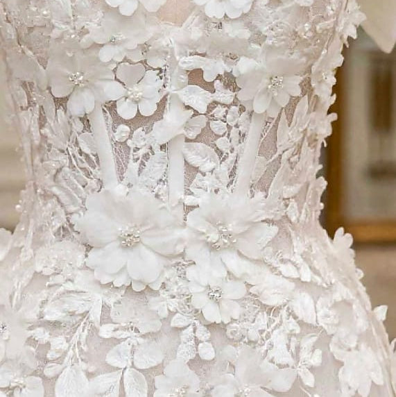 White floral lace wedding dress bodice with 3D floral appliqué and beaded detailing, shown in a close-up view.