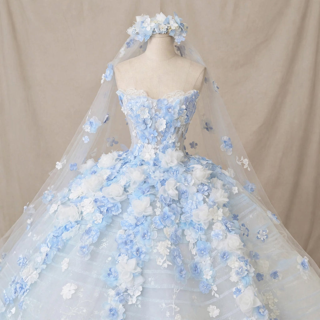 Light blue ball gown wedding dress with white and blue 3D floral appliqués, sheer corset bodice, and a matching floral cathedral veil displayed on a mannequin.

