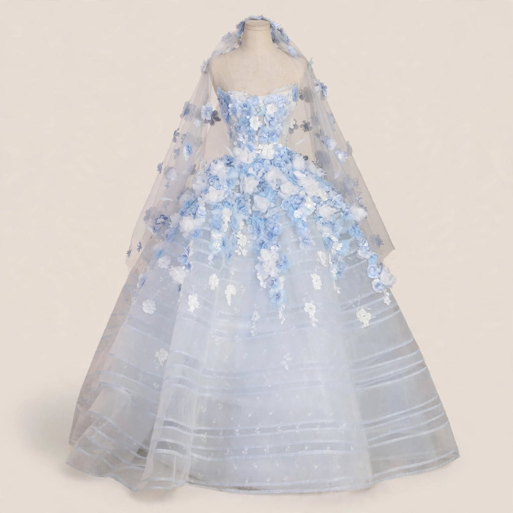 Light blue ball gown wedding dress with white and blue 3D floral appliqués, sheer corset bodice, and a matching floral cathedral veil displayed on a mannequin.

