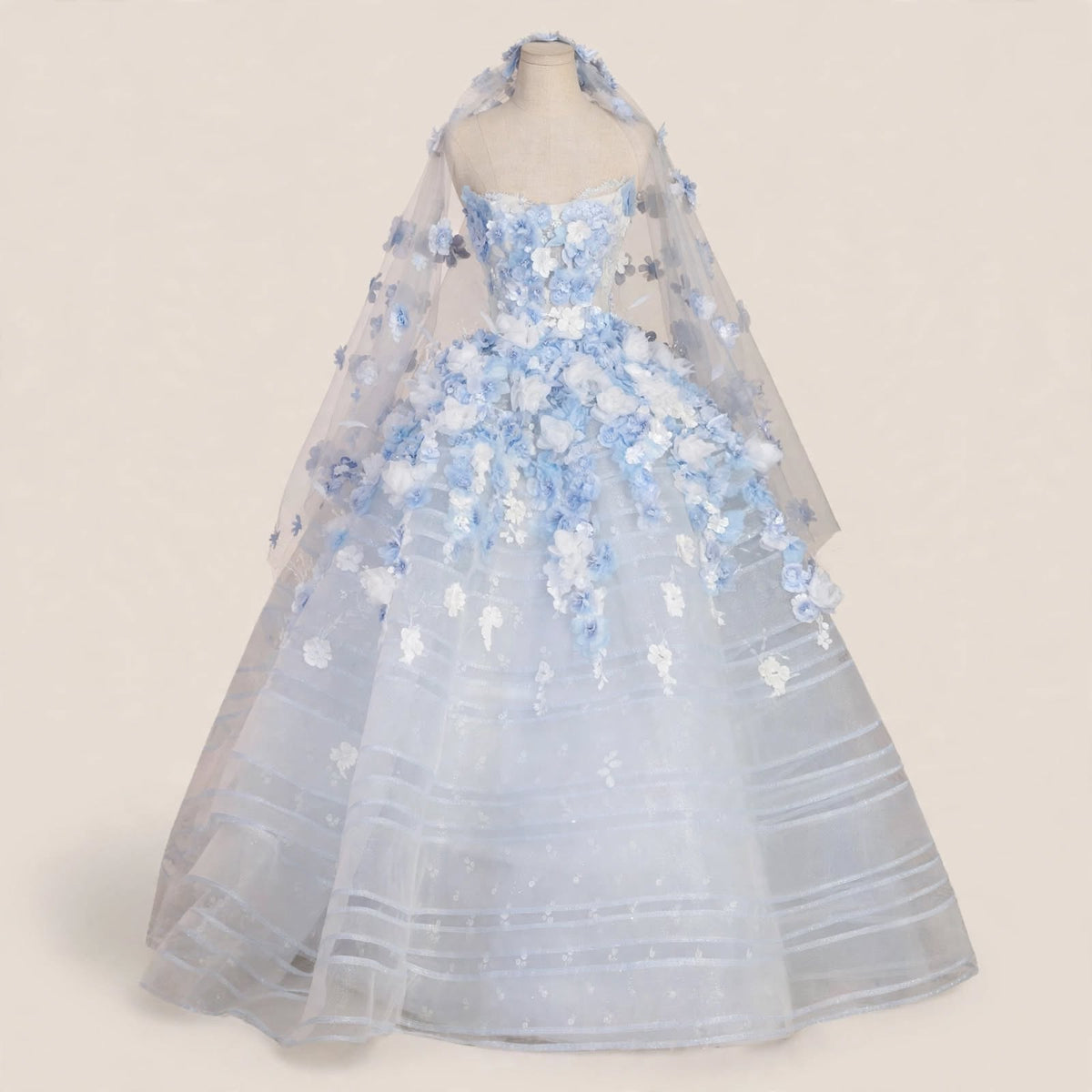 Light blue ball gown wedding dress with white and blue 3D floral appliqués, sheer corset bodice, and a matching floral cathedral veil displayed on a mannequin.

