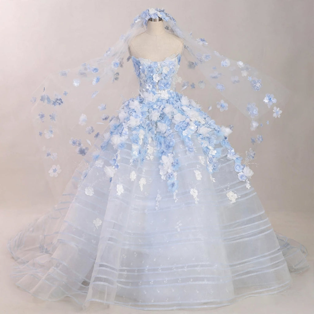 Light blue ball gown wedding dress with white and blue 3D floral appliqués, sheer corset bodice, and a matching floral cathedral veil displayed on a mannequin.

