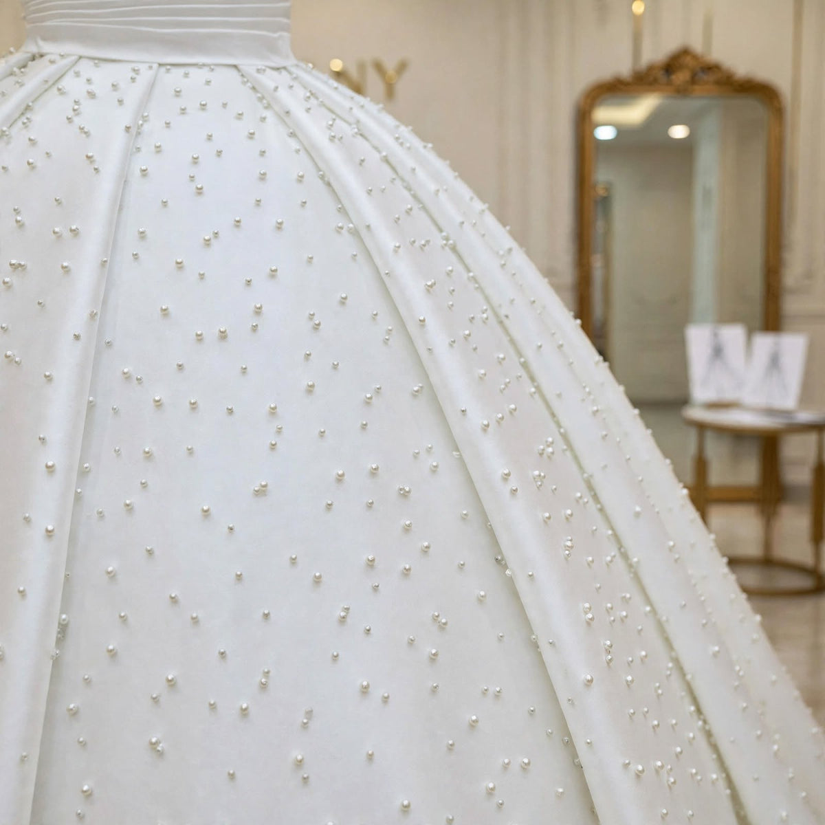 Close-up of the pleated satin skirt scattered with pearls on the Marguerite modest wedding dress.