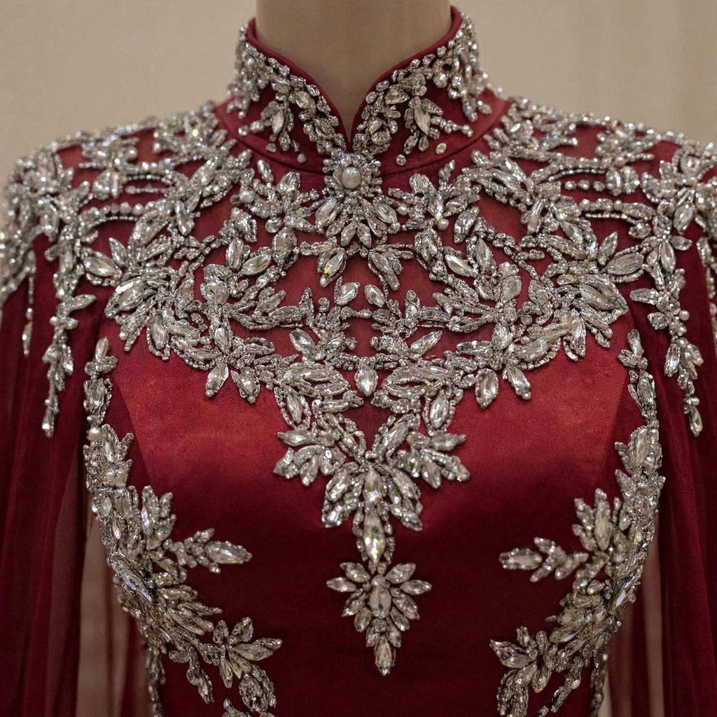 A close-up of a high-neck, long-sleeved red dress or gown on a mannequin, heavily decorated with intricate silver beading and crystal embellishments across the bodice and shoulders.