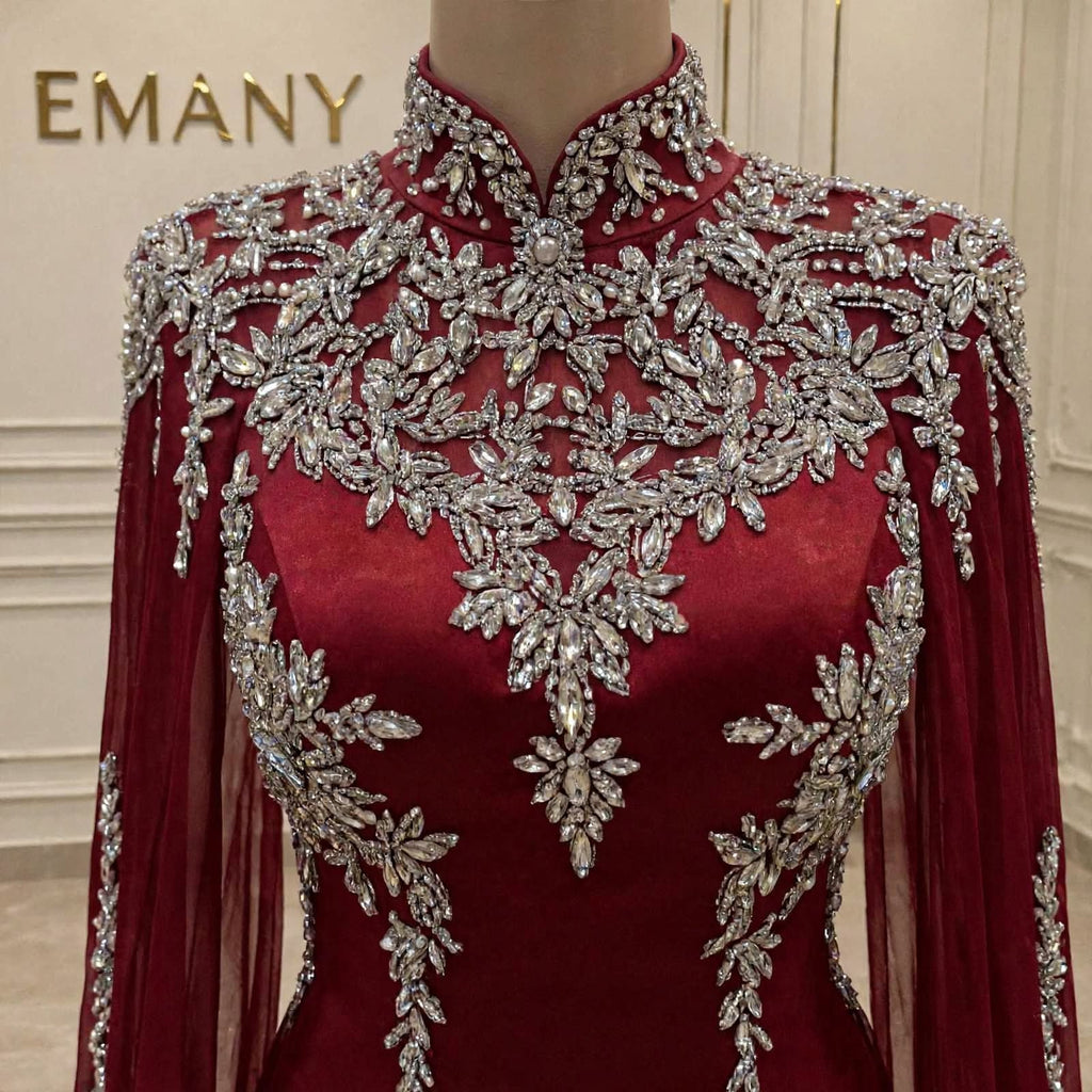 A close-up of a high-neck, long-sleeved burgundy dress displayed on a mannequin. The dress features extensive silver beaded floral embroidery across the bodice, shoulders, and sleeves.
