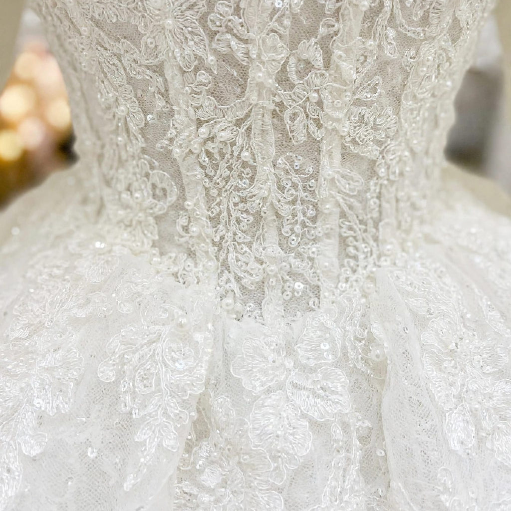 Macro detail of the exquisite hand-sewn lace, floral embroidery, and sparkling beads on the Victoria royal wedding dress by EMANY.


