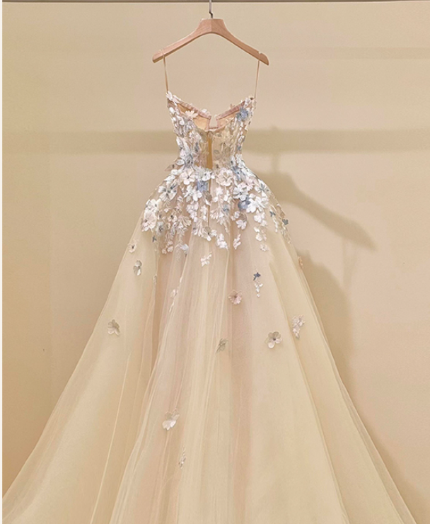 Champagne ball gown wedding dress with spaghetti straps and 3D floral appliqués in white and blue displayed on a hanger.

